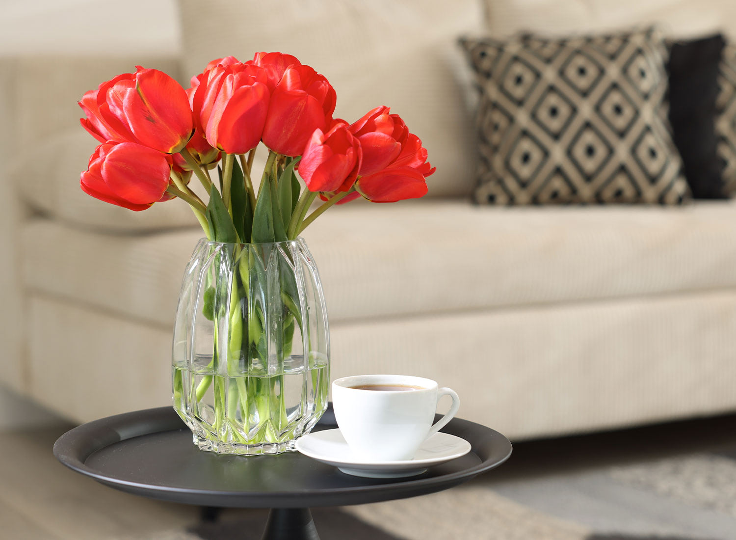 Red tulips arranged in glass vase on a black coffee table in cozy living room