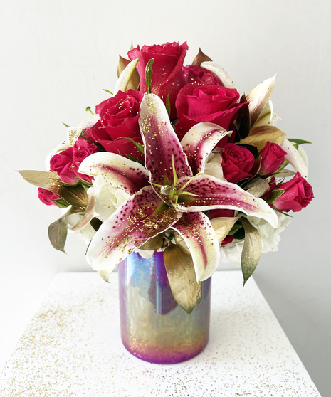 red roses and lilies in bouquet with gold leaves in purple vase