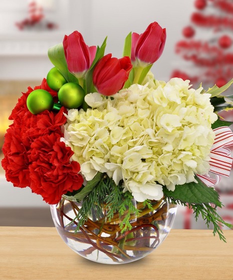 Red and white flowers in a clear glass bowl accented with holiday ornaments