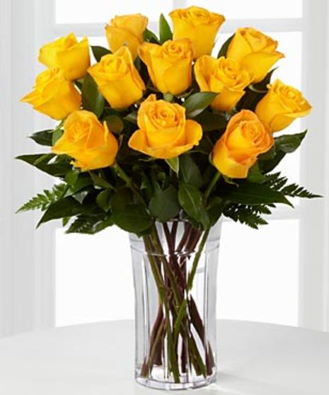 One dozen yellow roses in a clear glass vase with baby's breath.