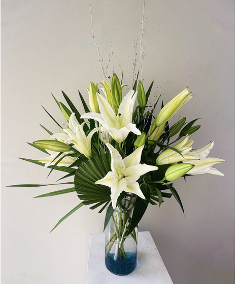 lilies and seaside greenery like palm leaves in blue stoned vase