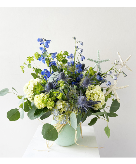 Stargazer lilies and hydrangea with seashells and starfish in a glass cube vase.