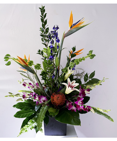 Orchids and other assorted tropical flowers  in a charming container.