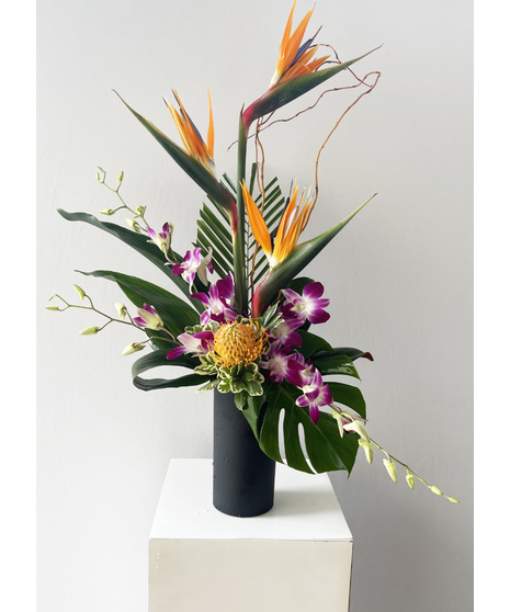 Orange lilies, mokara orchids, green kermit button mums and birds of paradise in a glass vase.