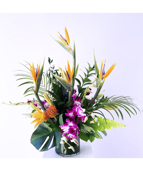 Orange lilies, mokara orchids, green kermit button mums and birds of paradise in a glass vase.