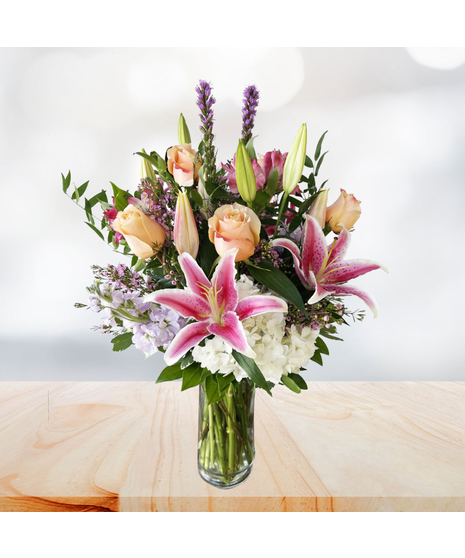 Peach, pink and white flowers in a clear glass cylinder vase.