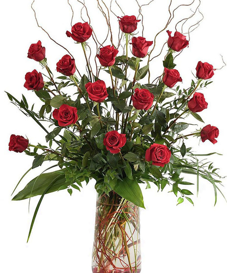 Red roses, greenery and curly willow in a clear glass vase.